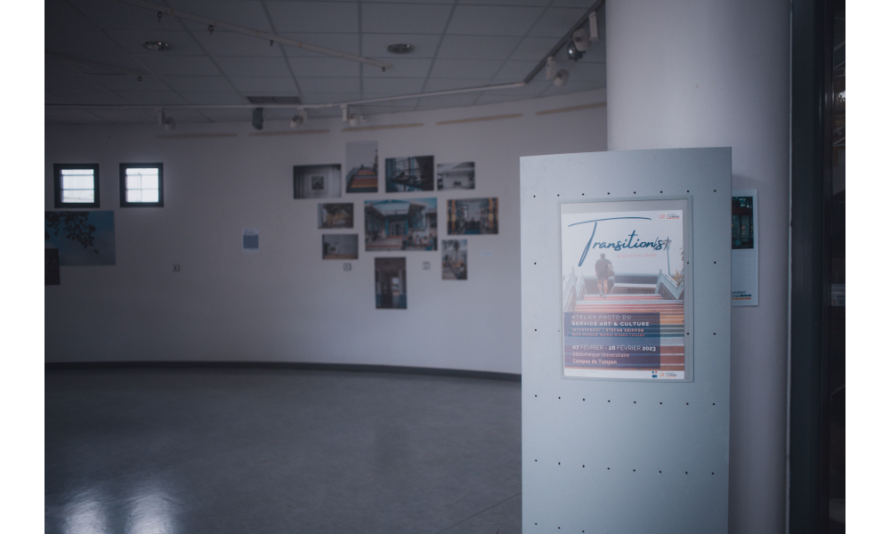 In the background, photos hanging on a wall. In the foreground, a panel with the exhibition poster.