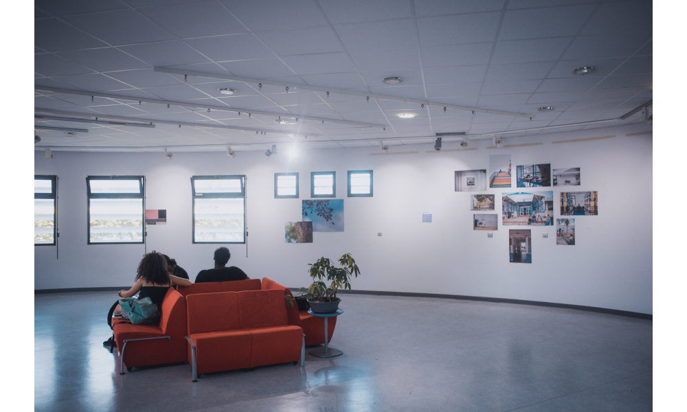 Exhibition visitors sitting on a sofa in the middle of the room, facing the photos on the wall.