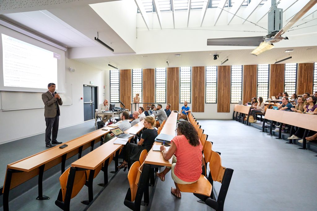 Photo en plan large de la pré-rentrée des étudiants du second cycle de médecine. 
Les étudiants sont de dos, assis, et font face au Président de l'université, Frédéric MIRANVILLE, debout devant un écran pendant sa prise de parole