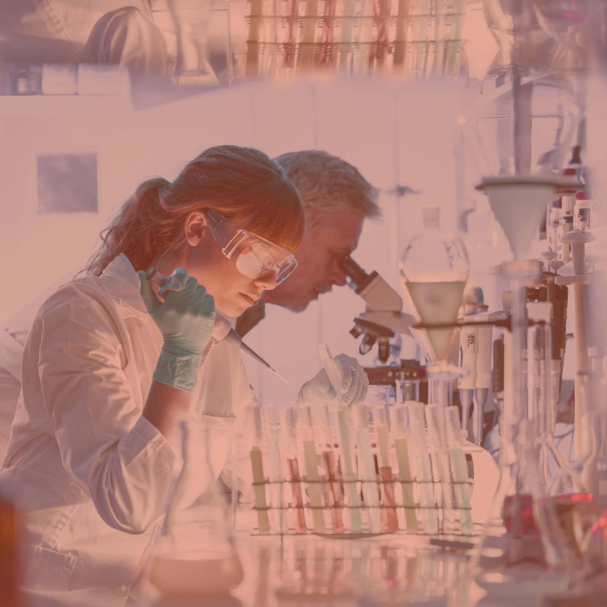 Deux chercheurs en blouse, l'une portant des lunettes de protection, l'autre observant au microscope dans un laboratoire.