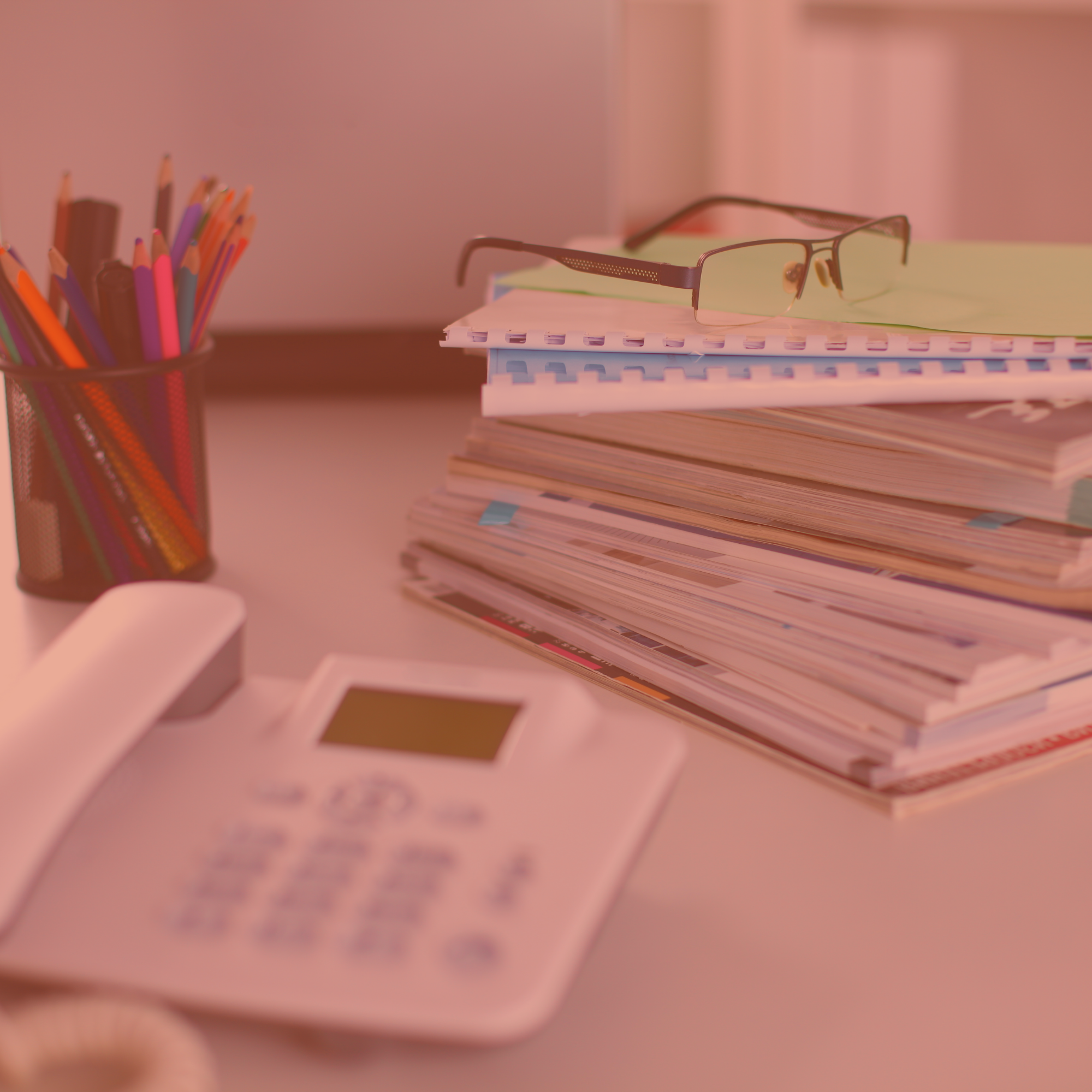 Bureau avec un téléphone fixe, une pile de dossiers, des lunettes et un pot à crayons.