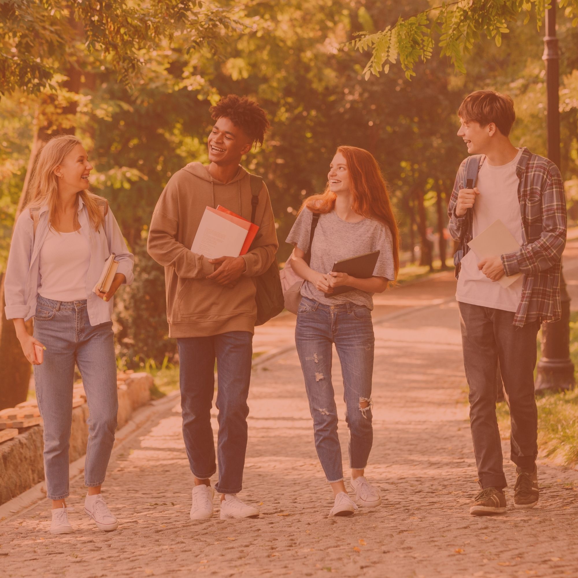 Image d'illustration : quatre étudiants qui marchent en souriant, livres et sacs à la main
