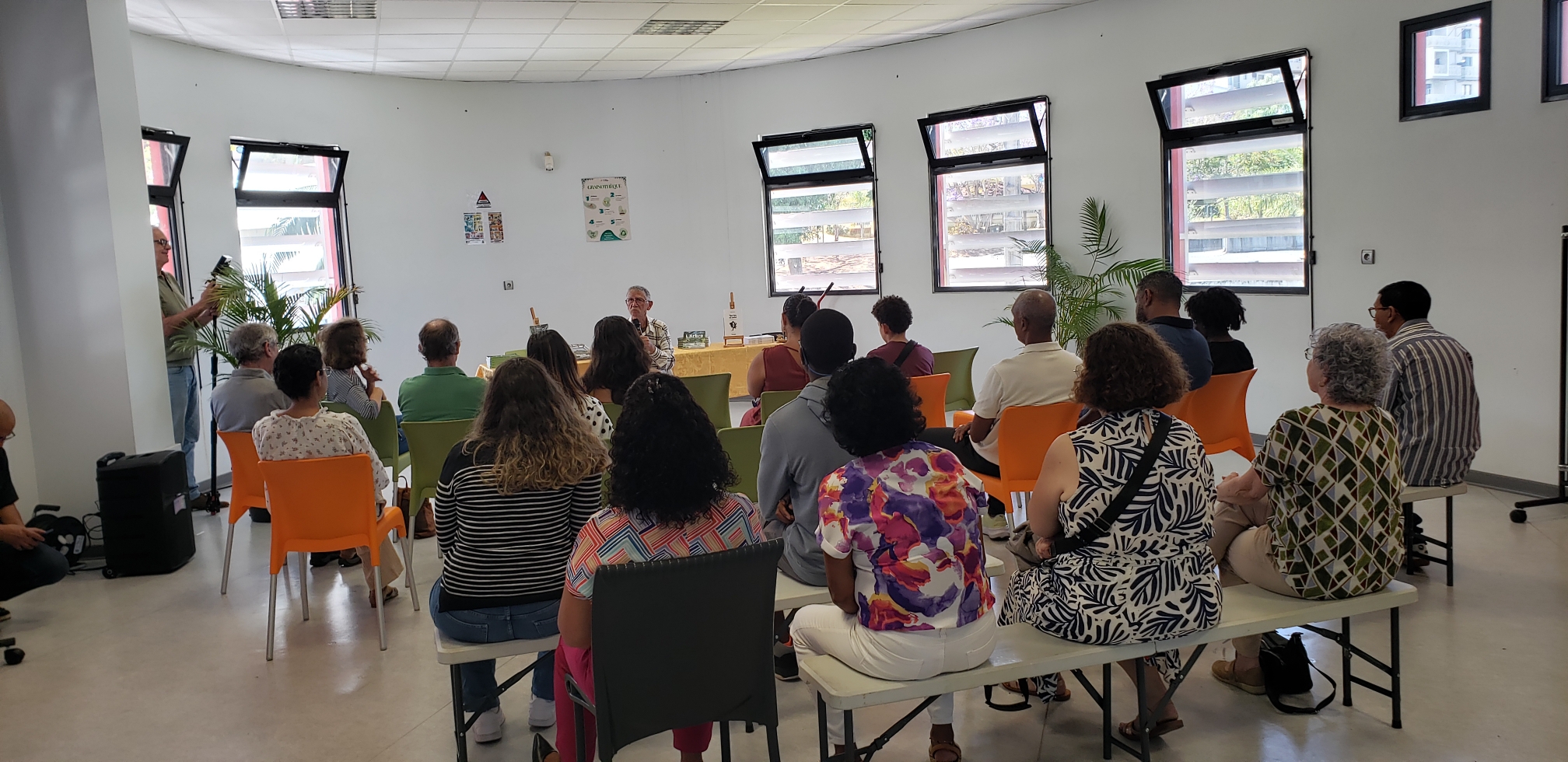 Vue d'ensemble d'une présentation dans une salle semi-circulaire lumineuse devant un public assis.